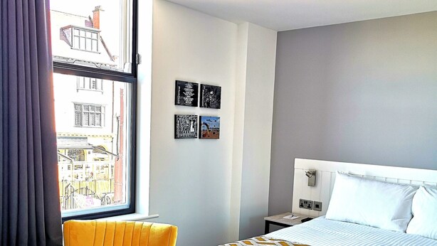 A hotel room with a bed, a chair, a window with curtains, and wall art. - Mode Hotel Lytham (Lytham St. Anne's)