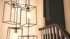 A staircase with a wooden handrail and a light fixture with multiple square frames and bulbs. - Mode Hotel Lytham (Lytham St. Anne's)