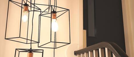 A staircase with a wooden handrail and a light fixture with multiple square frames and bulbs.