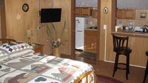Een kamer met een bed, een bureau, een televisie en een keukenruimte zichtbaar door een geopende deur.