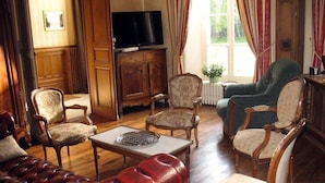 Un salón tradicional con muebles de madera, televisor y un ventanal con cortinas.