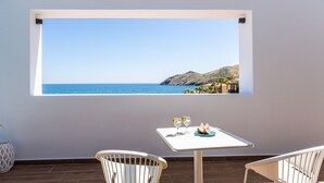 A balcony with a table and chairs, a view of the sea, and a window with a coastal landscape. - Wave Villa, Seaside Living &  Your Own Beach Spot (Panormos in Rethymno)