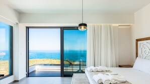 A modern hotel room with a large bed, a view of the sea, and a balcony with a chair. - Wave Villa, Seaside Living &  Your Own Beach Spot (Panormos in Rethymno)