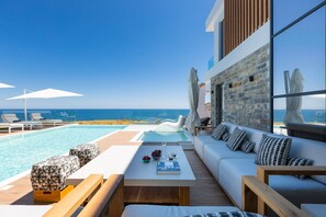 Un área lounge moderna al aire libre con piscina, mobiliario y vistas al océano.