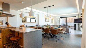 A modern kitchen with a central island, bar stools, pendant lighting, and a dining area with chairs and a table. - Wave Villa, Seaside Living &  Your Own Beach Spot (Panormos in Rethymno)