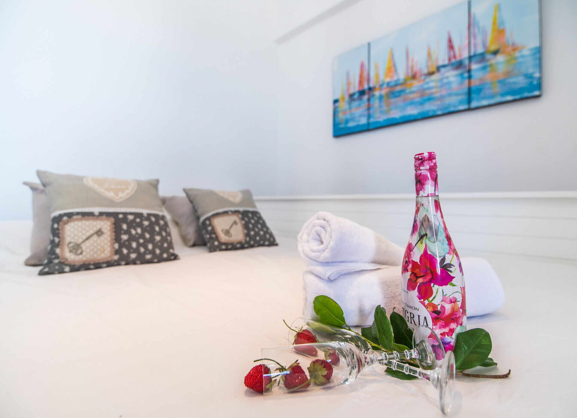 Un lit bien fait, avec des oreillers, une serviette enroulée, un flacon en verre décoré de motifs floraux et un bouquet de fraises.