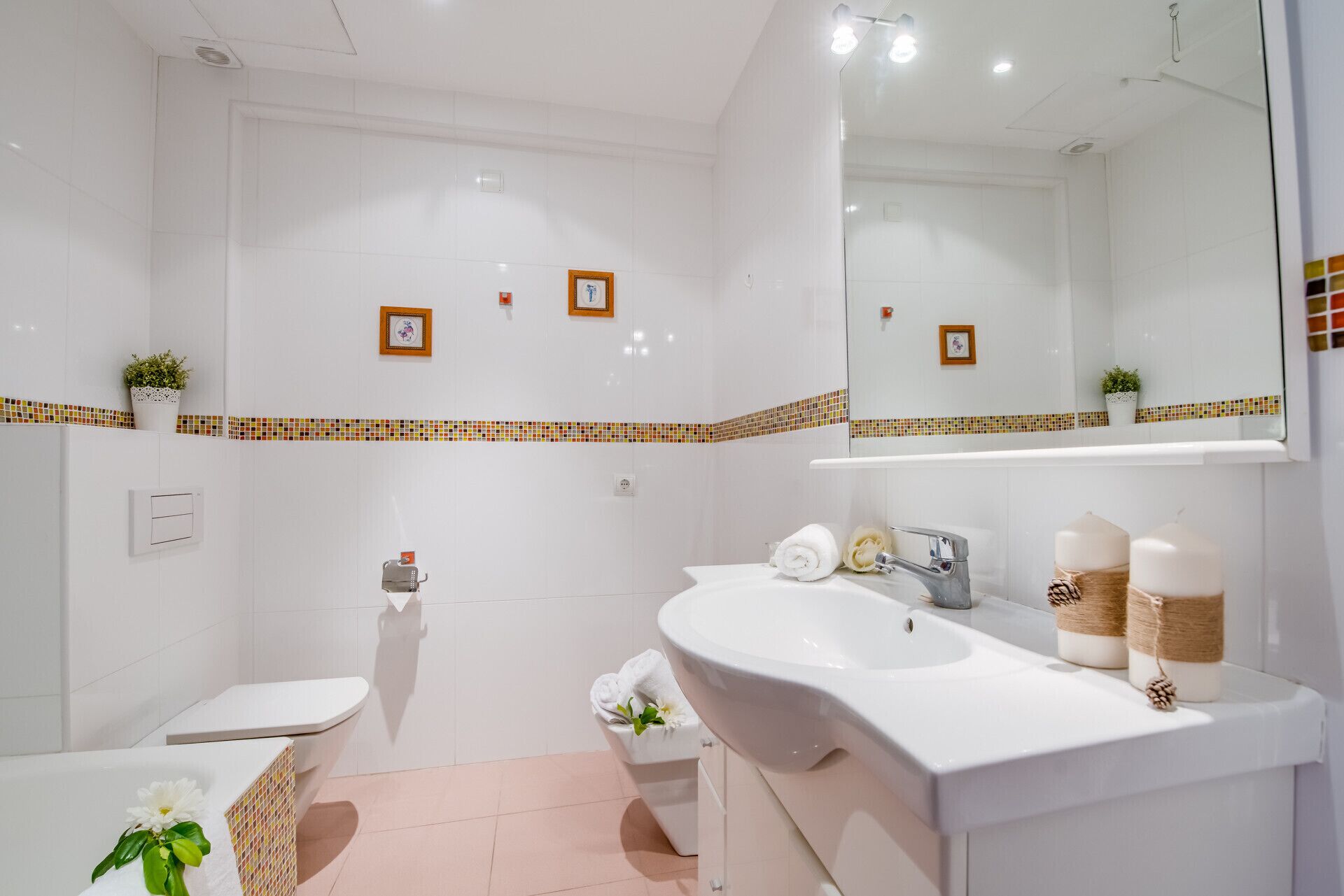 Ein modernes Badezimmer mit Waschbecken, Spiegel und Toilette in Weiß. Die Wände sind mit dekorativen Fliesen versehen und auf der Ablage steht eine kleine Pflanze.
