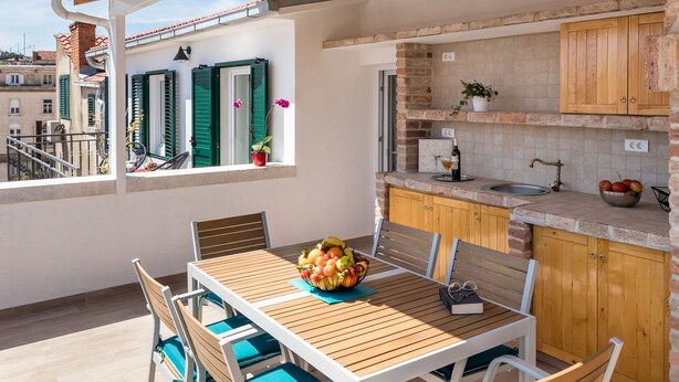 Una terraza en la azotea con una mesa y sillas de madera, una zona de cocina con armarios de madera y vistas a la ciudad.