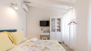 Un dormitorio con cama, escritorio, televisor, armario y perchero.