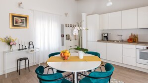 Una cocina moderna con armarios blancos, una mesa de comedor con sillas color turquesa y un frutero sobre la mesa.