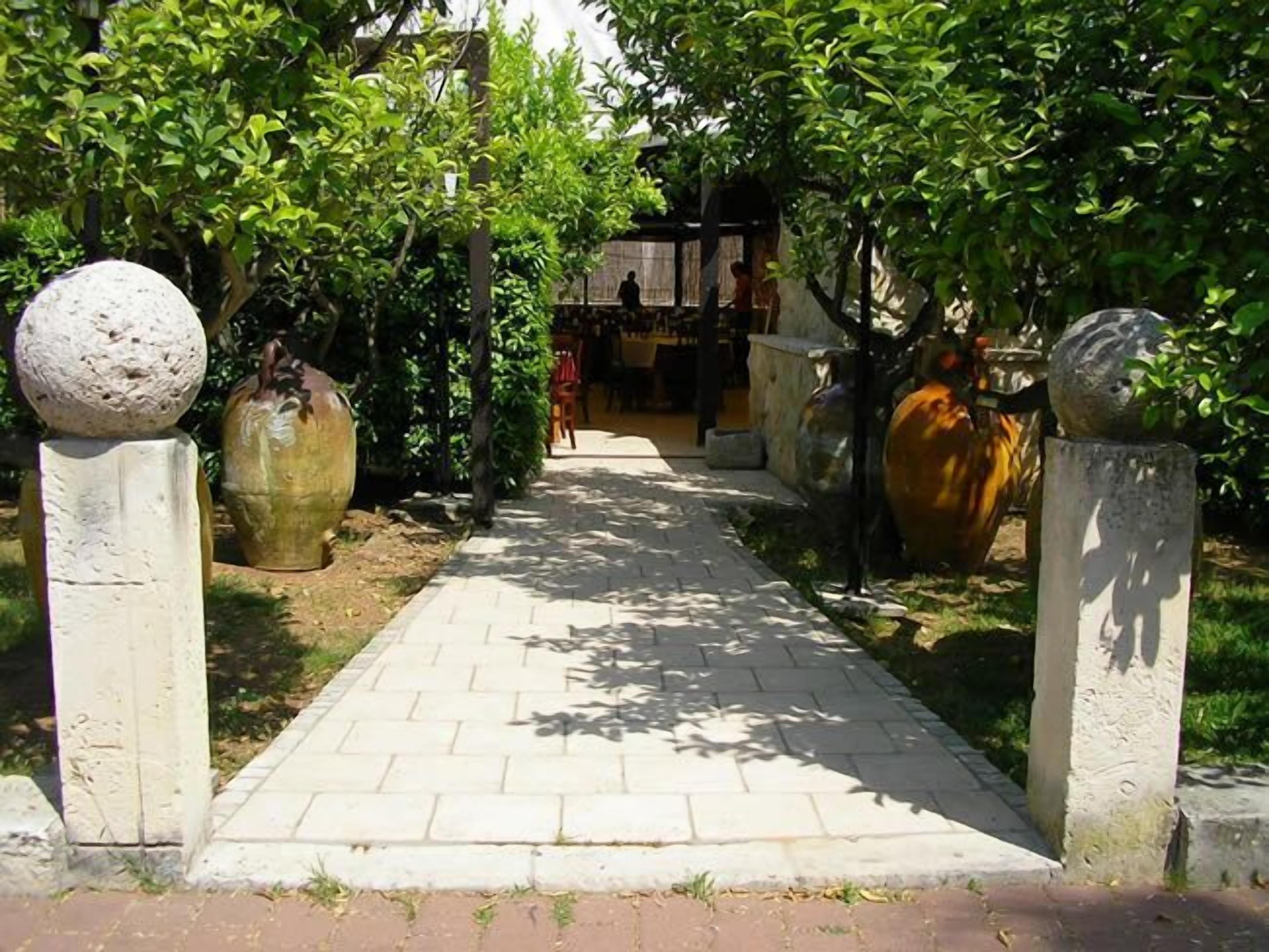 A pathway flanked by large decorative vases and spherical stone elements, leading to a building with a visible entrance.