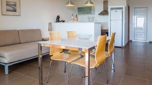 Moderni keittiö, jossa on ruokailutila. Keittiössä on valkoinen työtaso, ruostumattomasta teräksestä valmistetut kodinkoneet sekä lasitasoinen pöytä, jonka ympärillä on puiset tuolit.