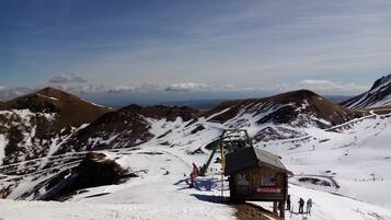 A mountain lodge with a ski lift, surrounded by snow-covered slopes and distant mountain ranges.