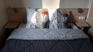 Een net opgemaakt bed met een grijs gebogen dekbedovertrek, twee kussens met een bloemenprint, en een houten hoofdbord.