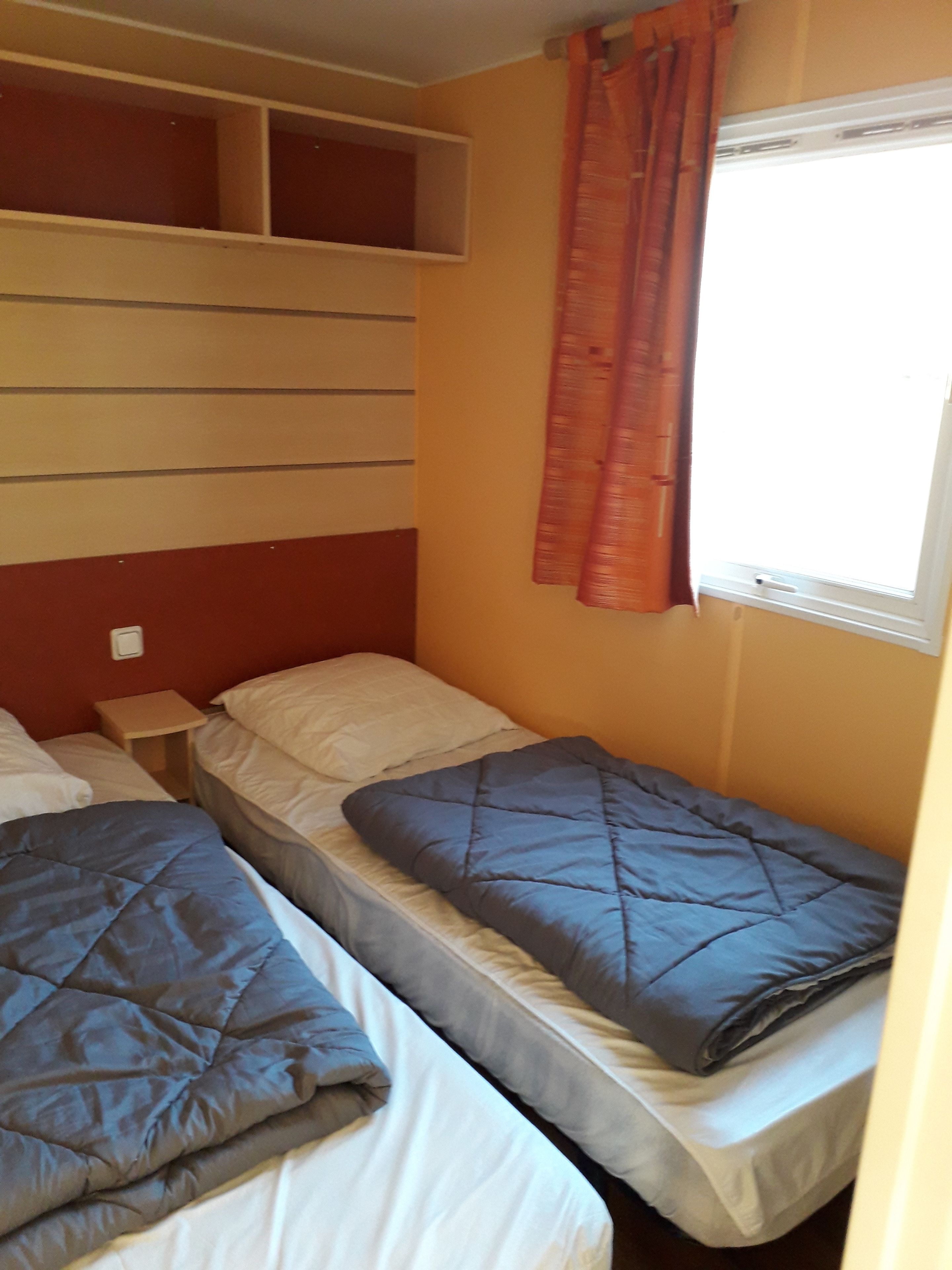 A room with two beds, a window with curtains, and a shelf unit.