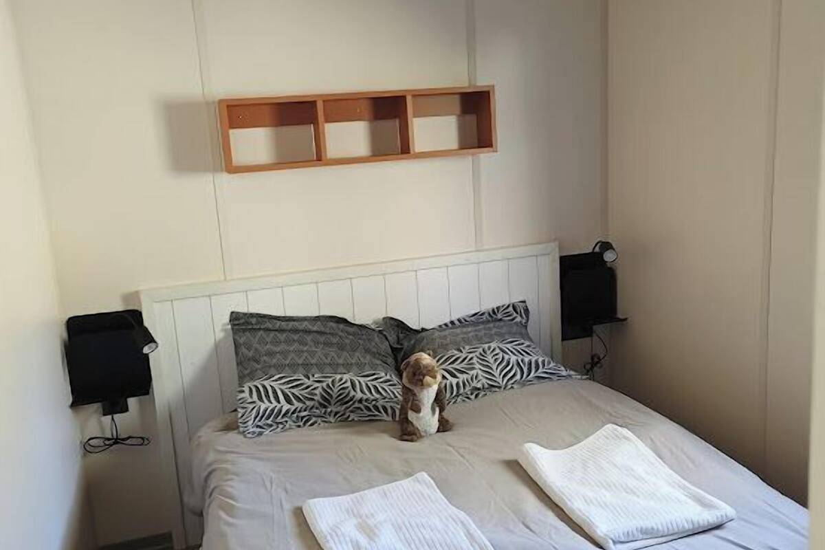 Une chambre à coucher comprenant un lit, des oreillers, une table de chevet, une étagère fixée au mur et un plafond avec des poutres en bois.