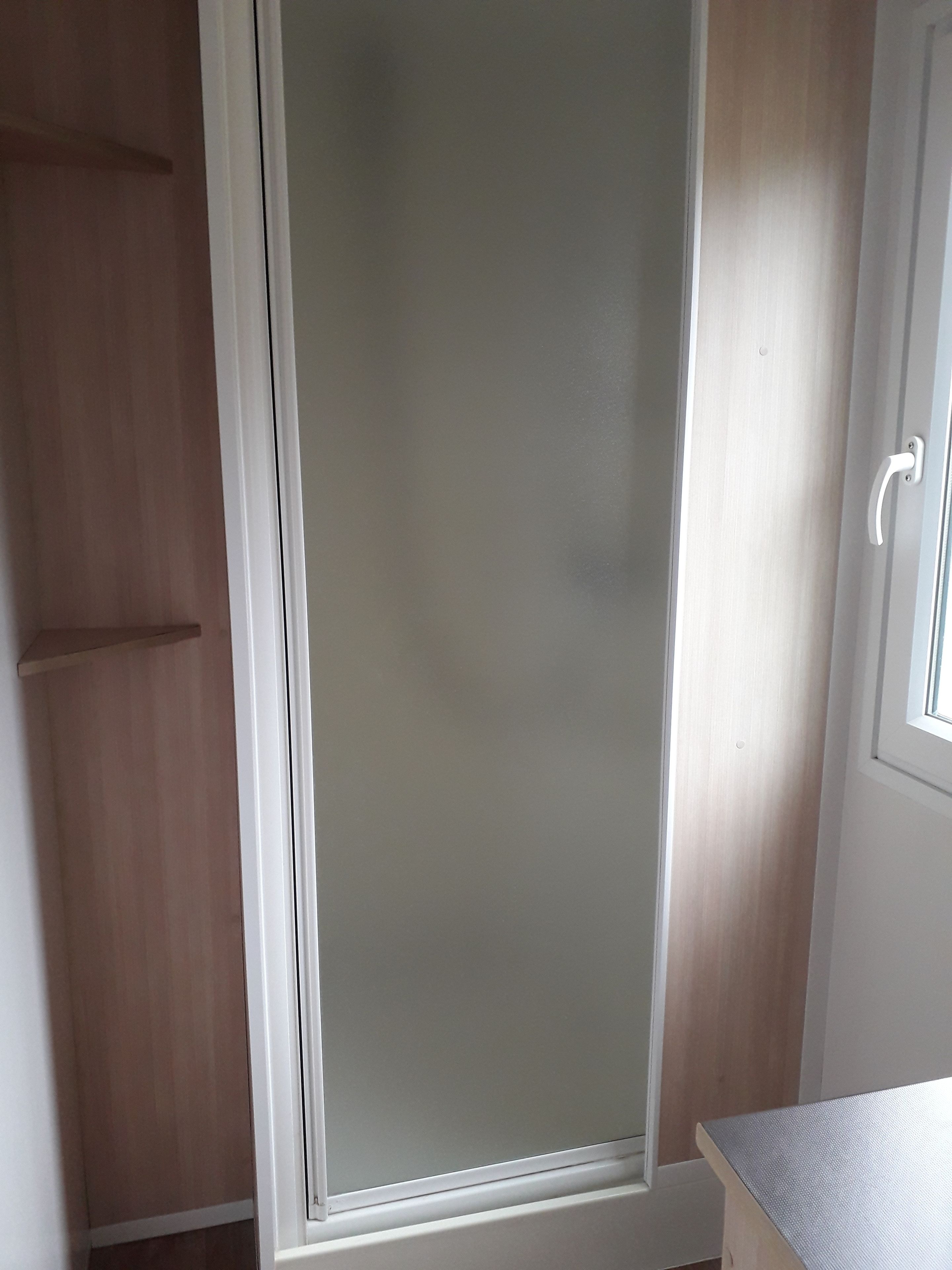 A room with a sliding door, a wooden wardrobe, and a small window.