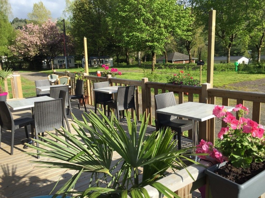 Un espace extérieur aménagé en terrasse, avec des tables et des chaises, entouré d’une plateforme en bois et de plantes en pot.