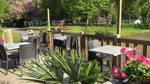 Een buitenpatio met tafels en stoelen, omgeven door een houten terras en plantenpotten.