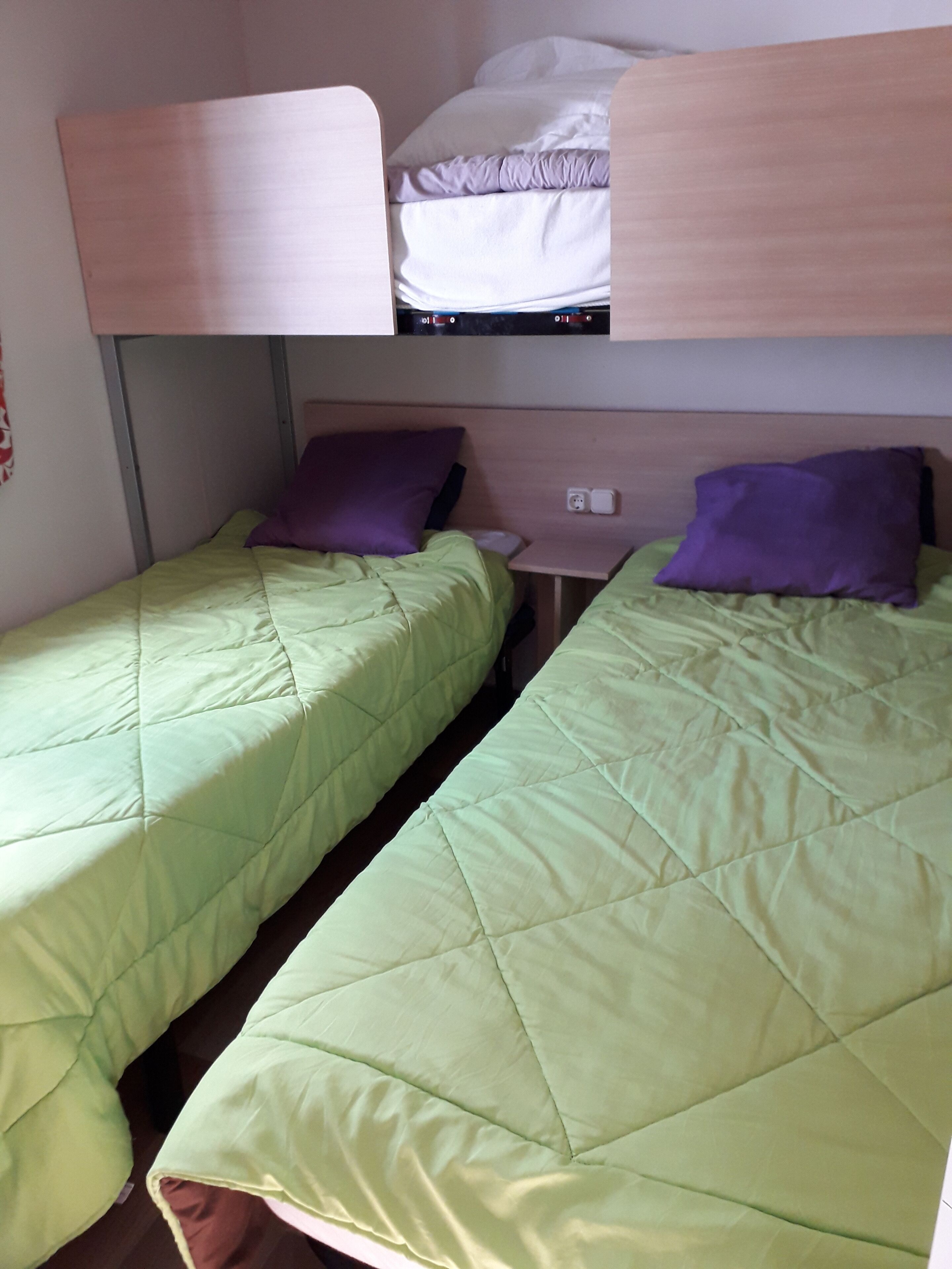 A bunk bed with two single beds, each with a green quilt and purple pillows.