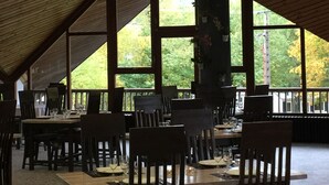 Een eetruimte met houten tafels en stoelen, grote ramen en hangende papieren lantaarns.
