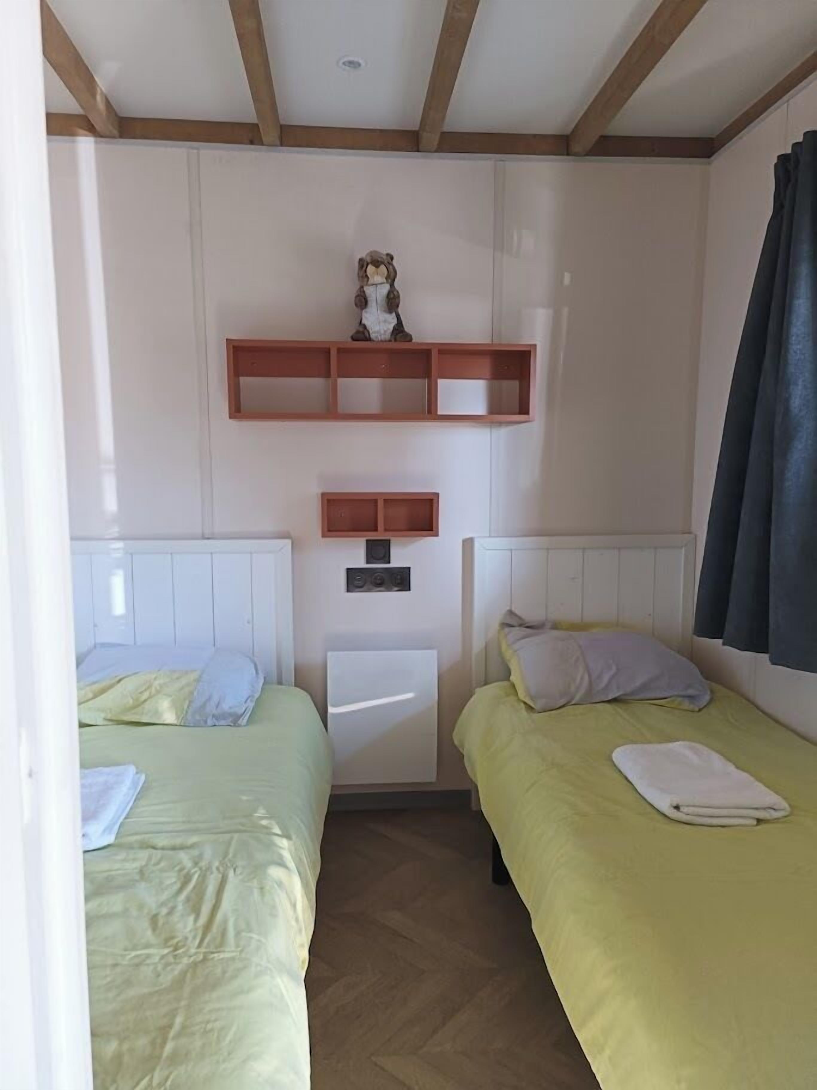 Una habitación con dos camas, un armario blanco pequeño y una estantería con un objeto decorativo.