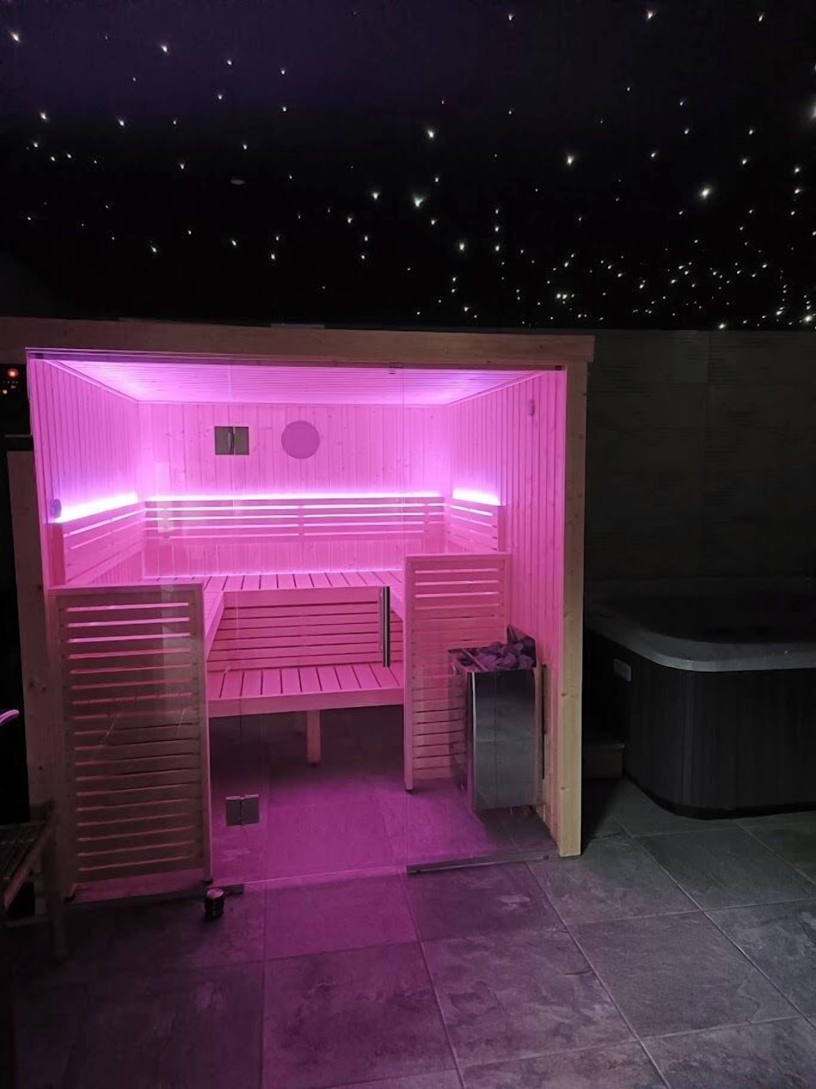 Een sauna met een bankje en een klein tafeltje, omgeven door een houten constructie met roze verlichting.
