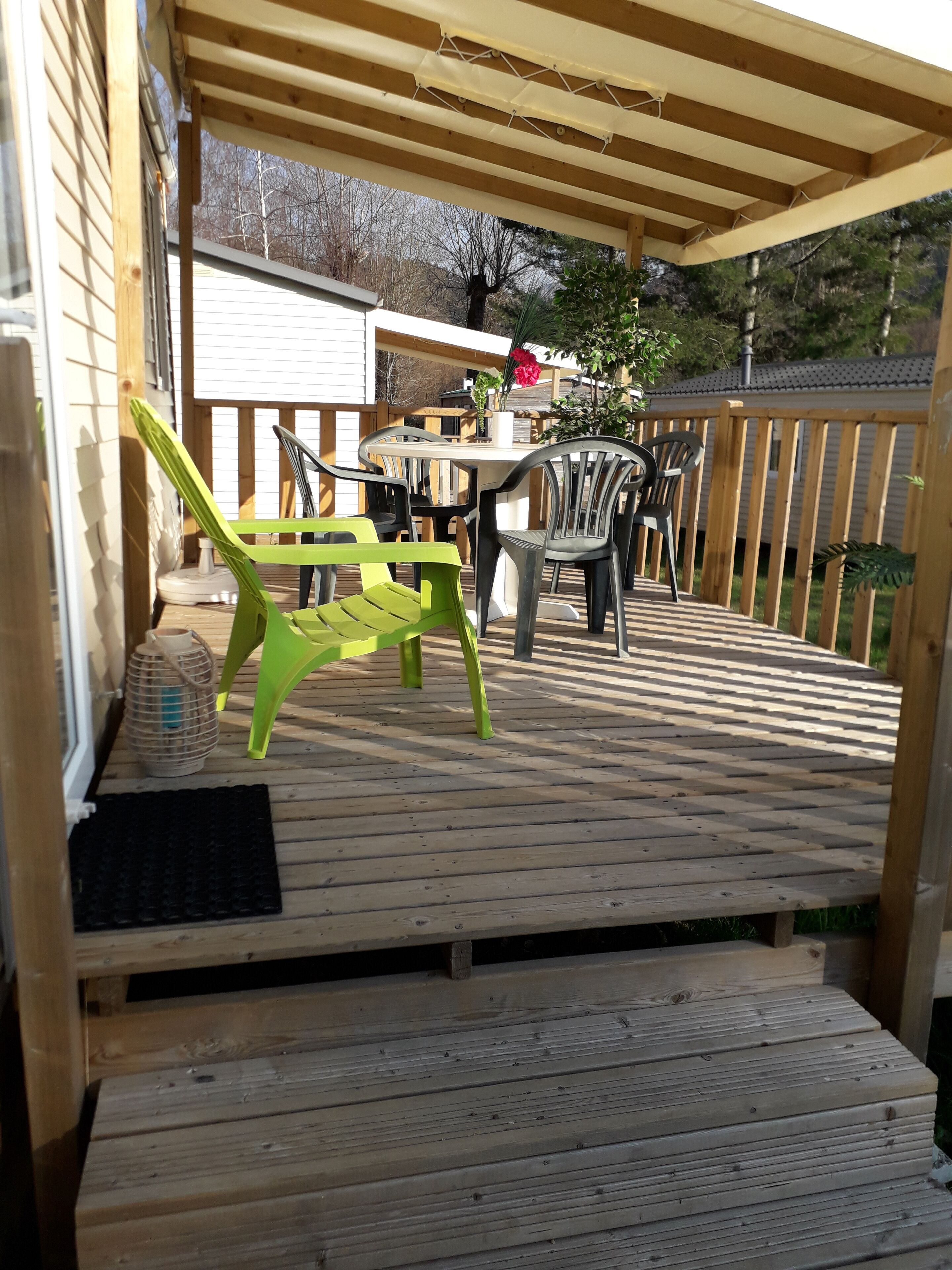 Eine Holzterrasse mit Tisch, Stühlen, einem Topfpflanzen und einem Hollerzaun.