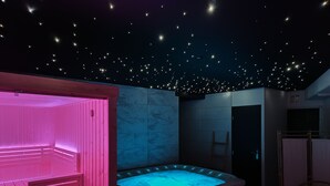 Een kamer met een jacuzzi, een houten sauna en een plafond met sterrenverlichting.