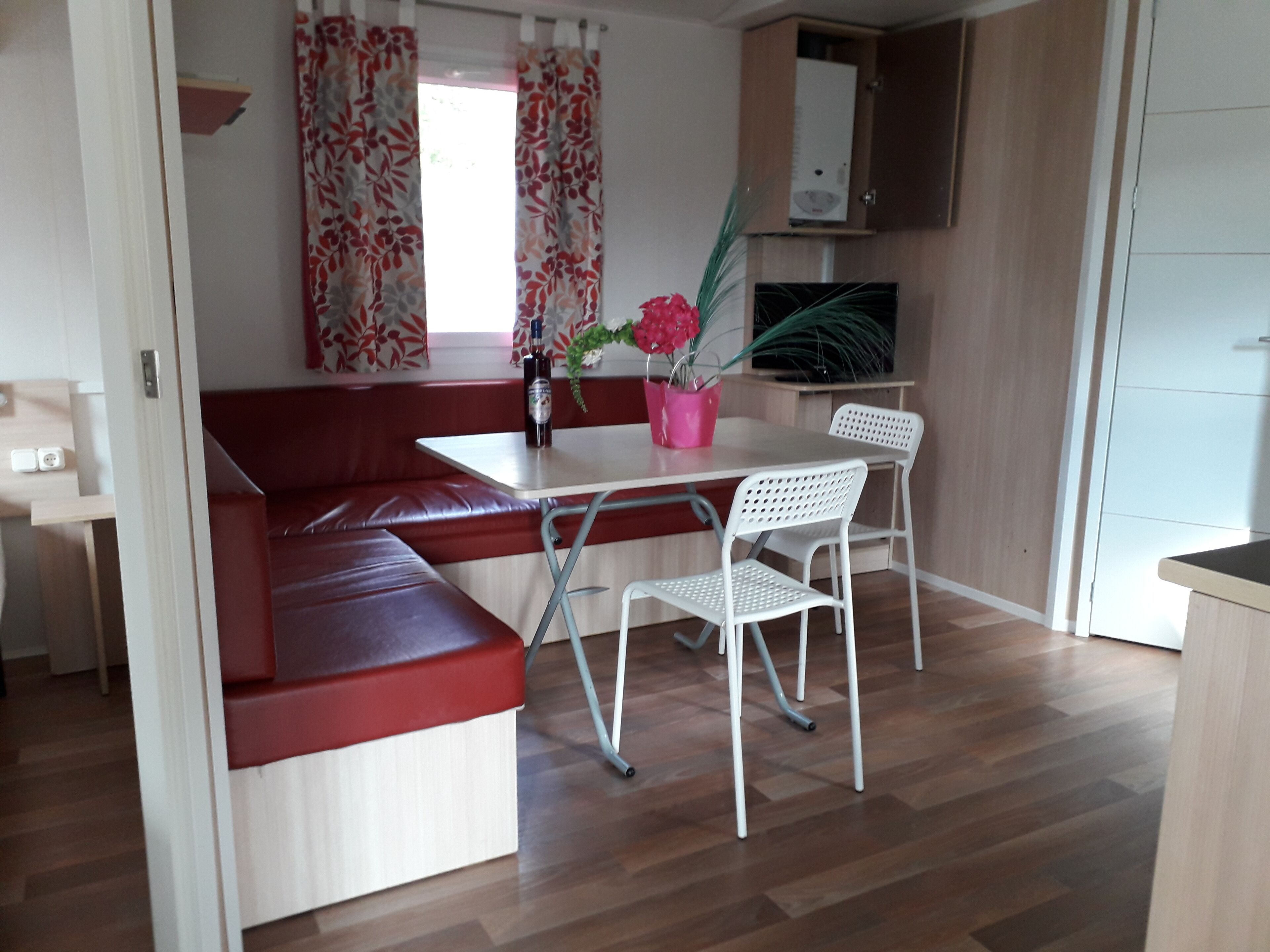 A compact living space with a red cushioned bench, a small dining table with two chairs, and a potted plant.