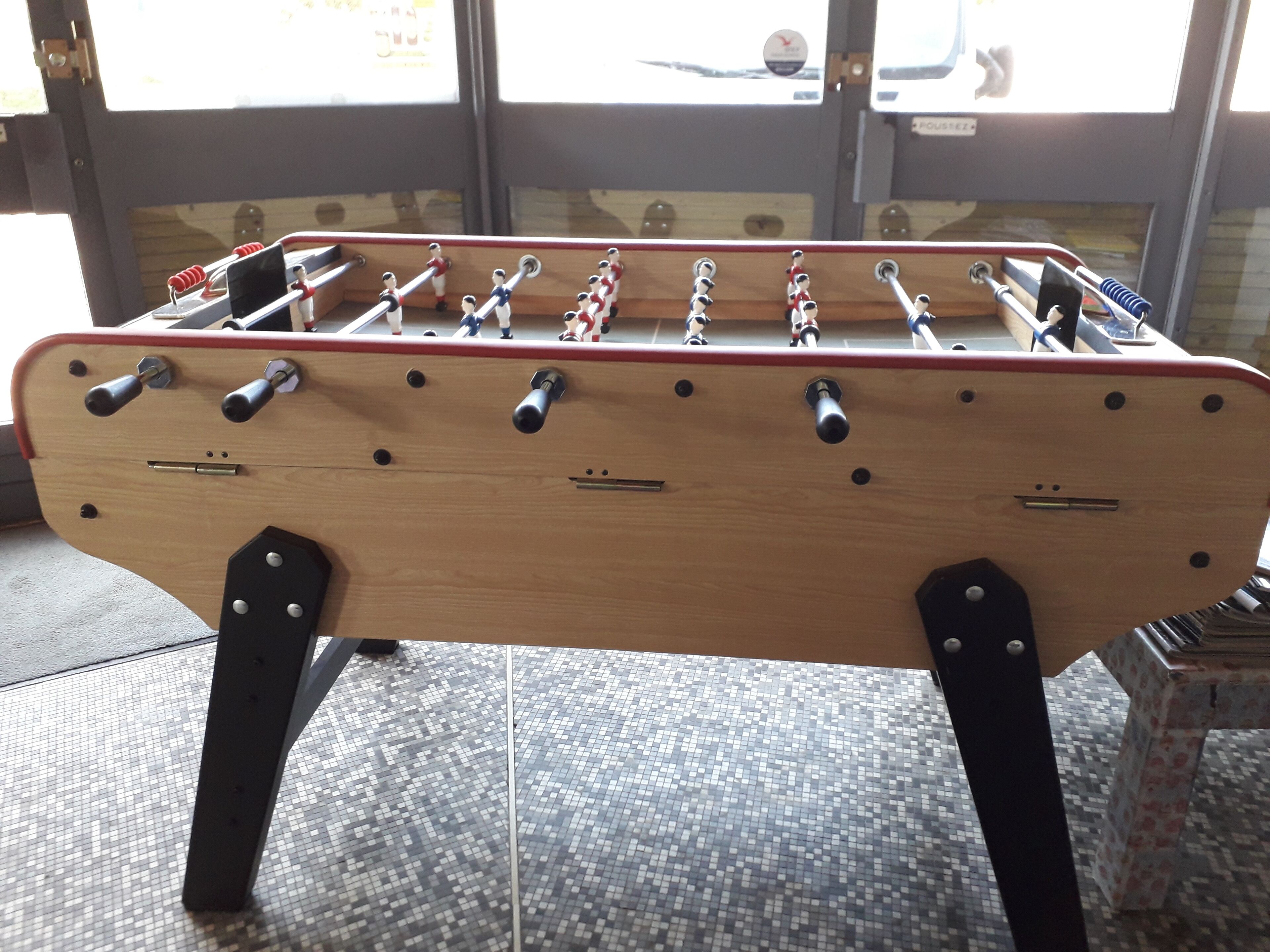 A wooden foosball table with metal rods and figures, set on a tiled floor.