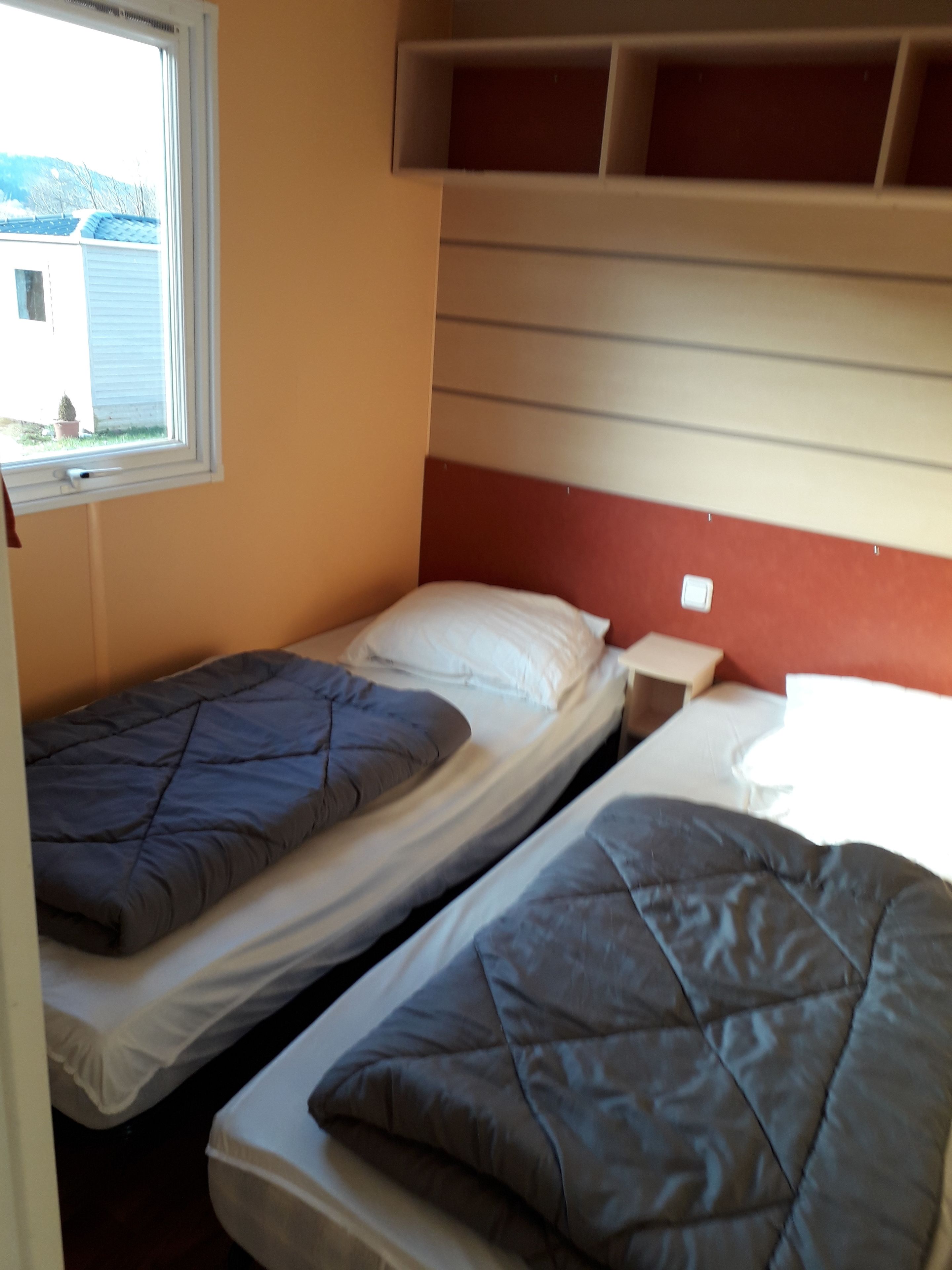 Une petite chambre compacte avec deux lits simples, une fenêtre et une étagère intégrée au-dessus des lits.