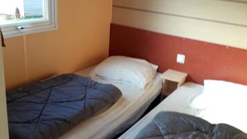 Une petite chambre compacte avec deux lits simples, une fenêtre et une étagère intégrée au-dessus des lits.