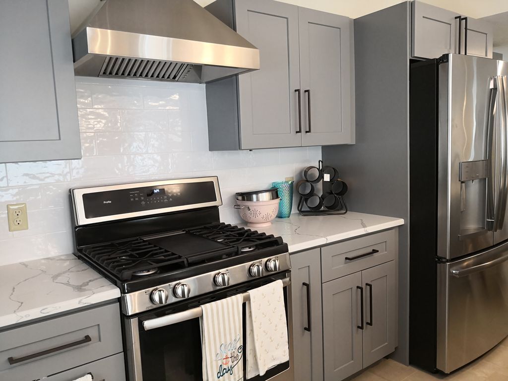 Une cuisine moderne avec des meubles gris, une cuisinière en acier inoxydable et un réfrigérateur.