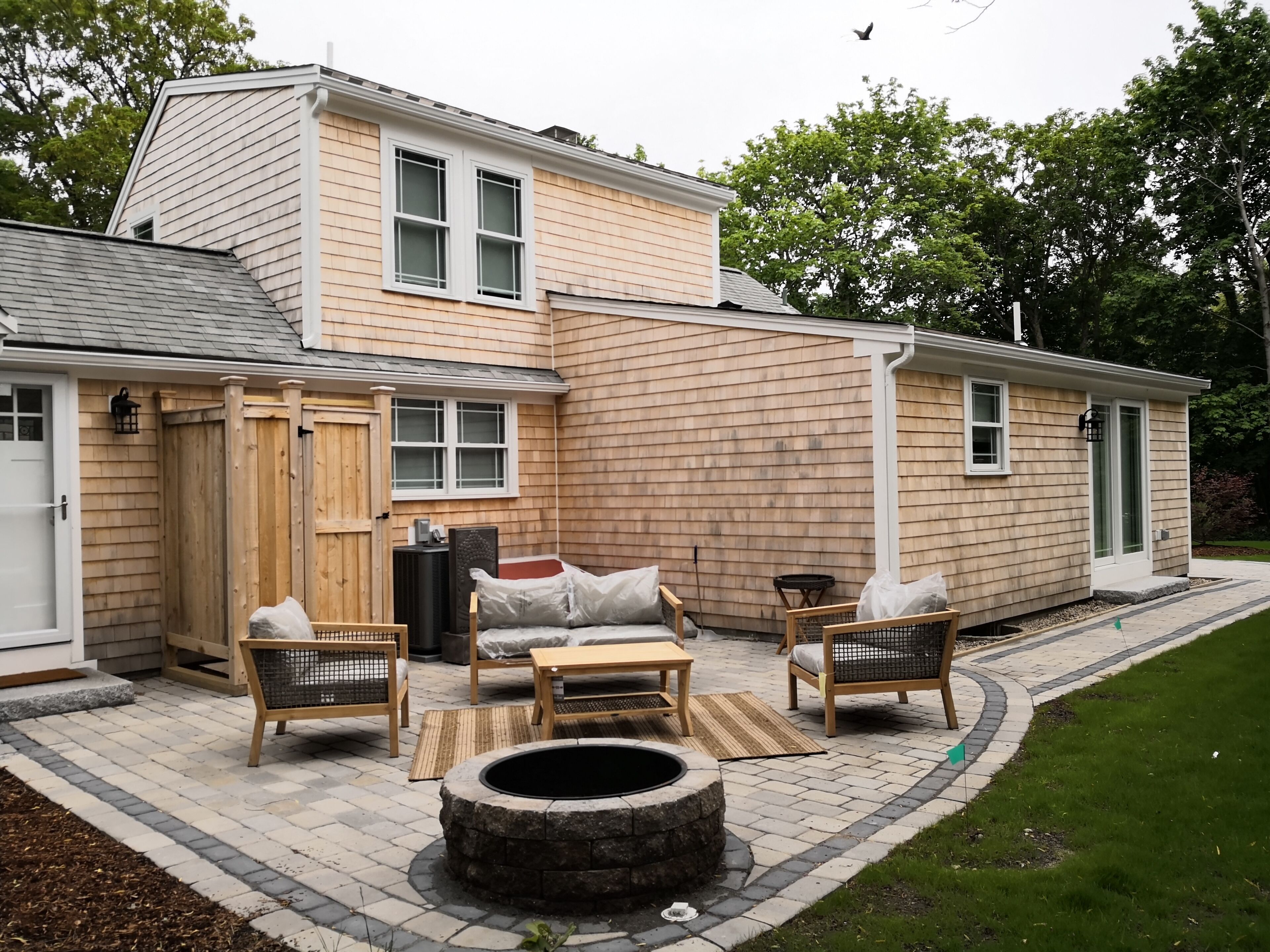Ein zweistöckiges Haus mit einer Terrasse, die Gartenmöbel, eine Feuerstelle und eine Holzterrasse bietet.