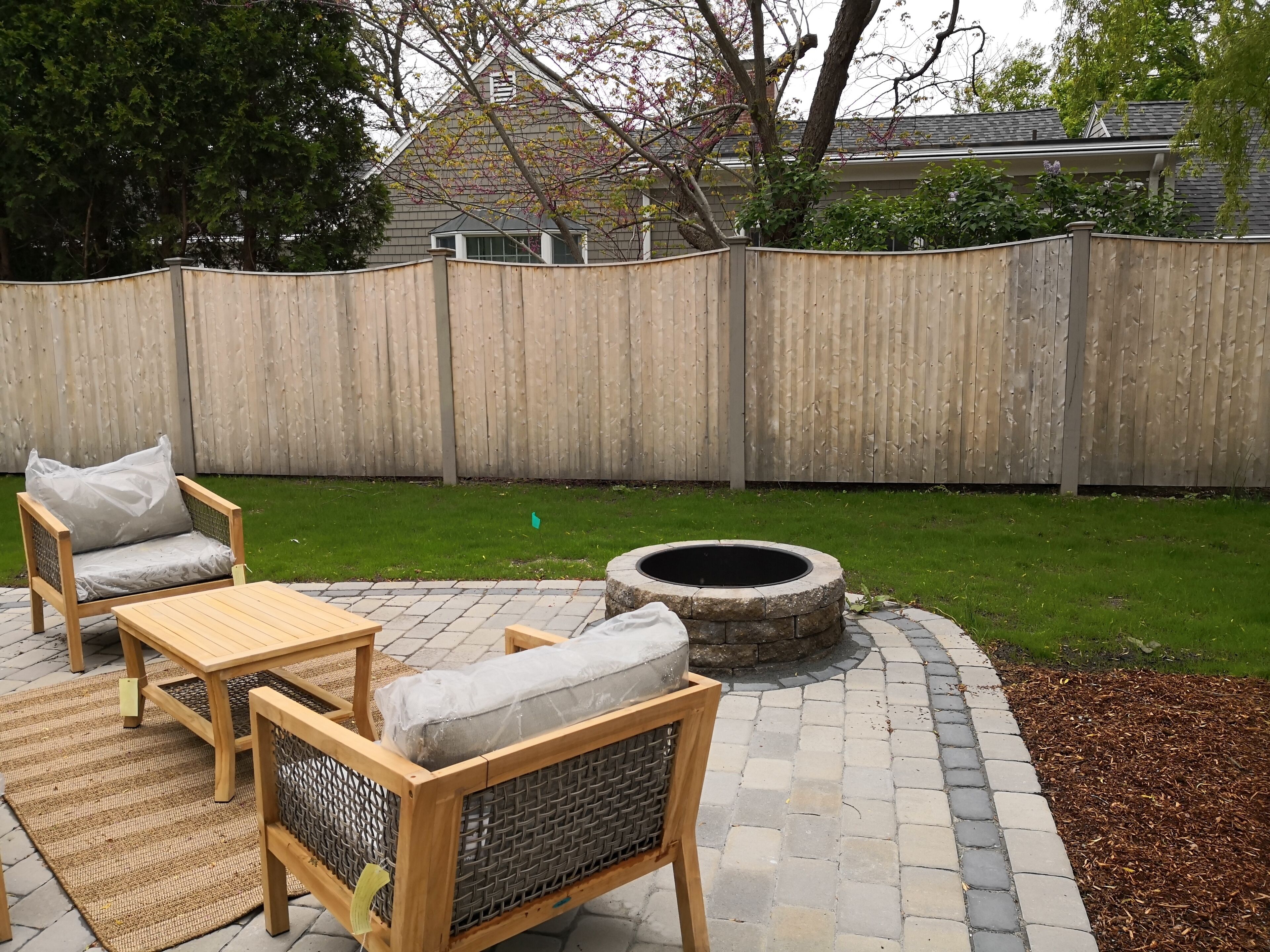 A patio area with a wooden table and chairs, a fire pit, and a wooden fence.
