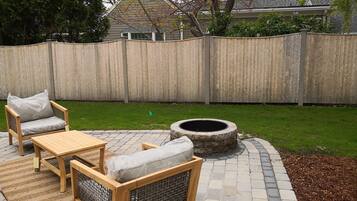 A patio area with a wooden table and chairs, a fire pit, and a wooden fence.
