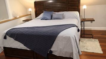 A neatly made bed with a dark blanket, two bedside lamps, and a wooden headboard.