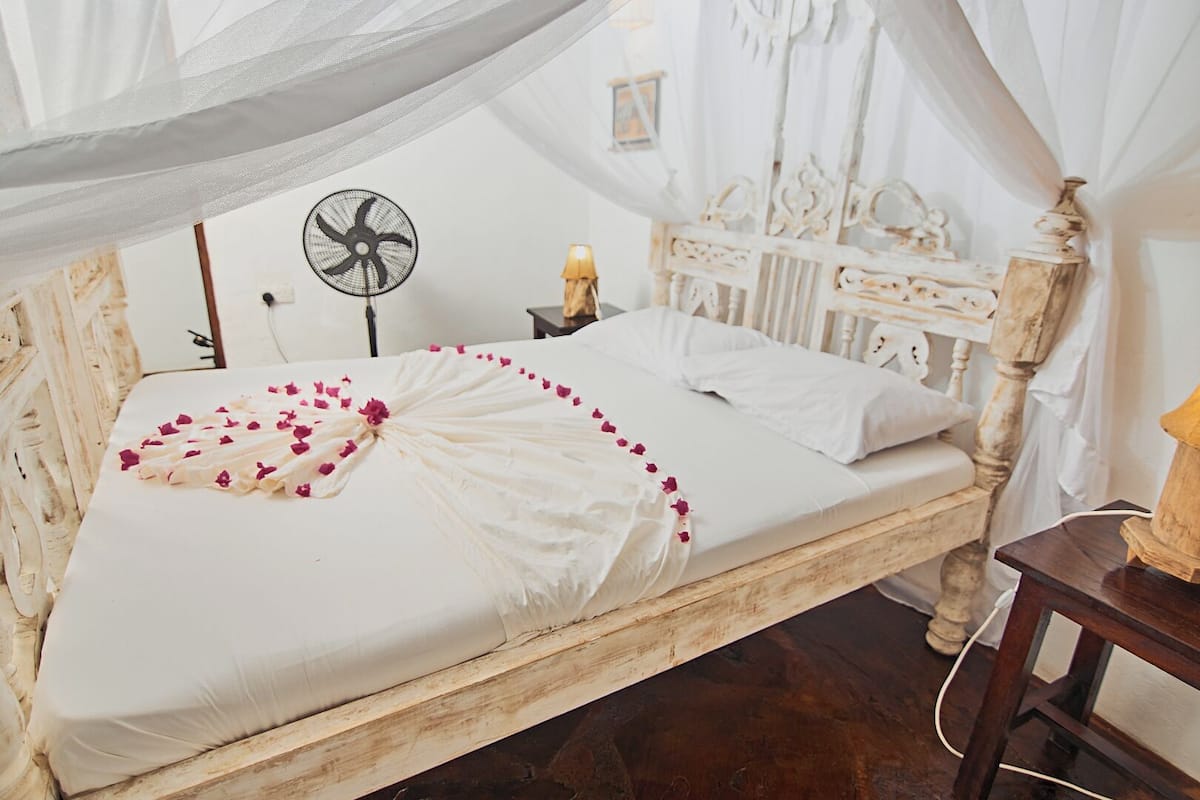 Una cama con dosel, sábanas blancas y pétalos de rosa.