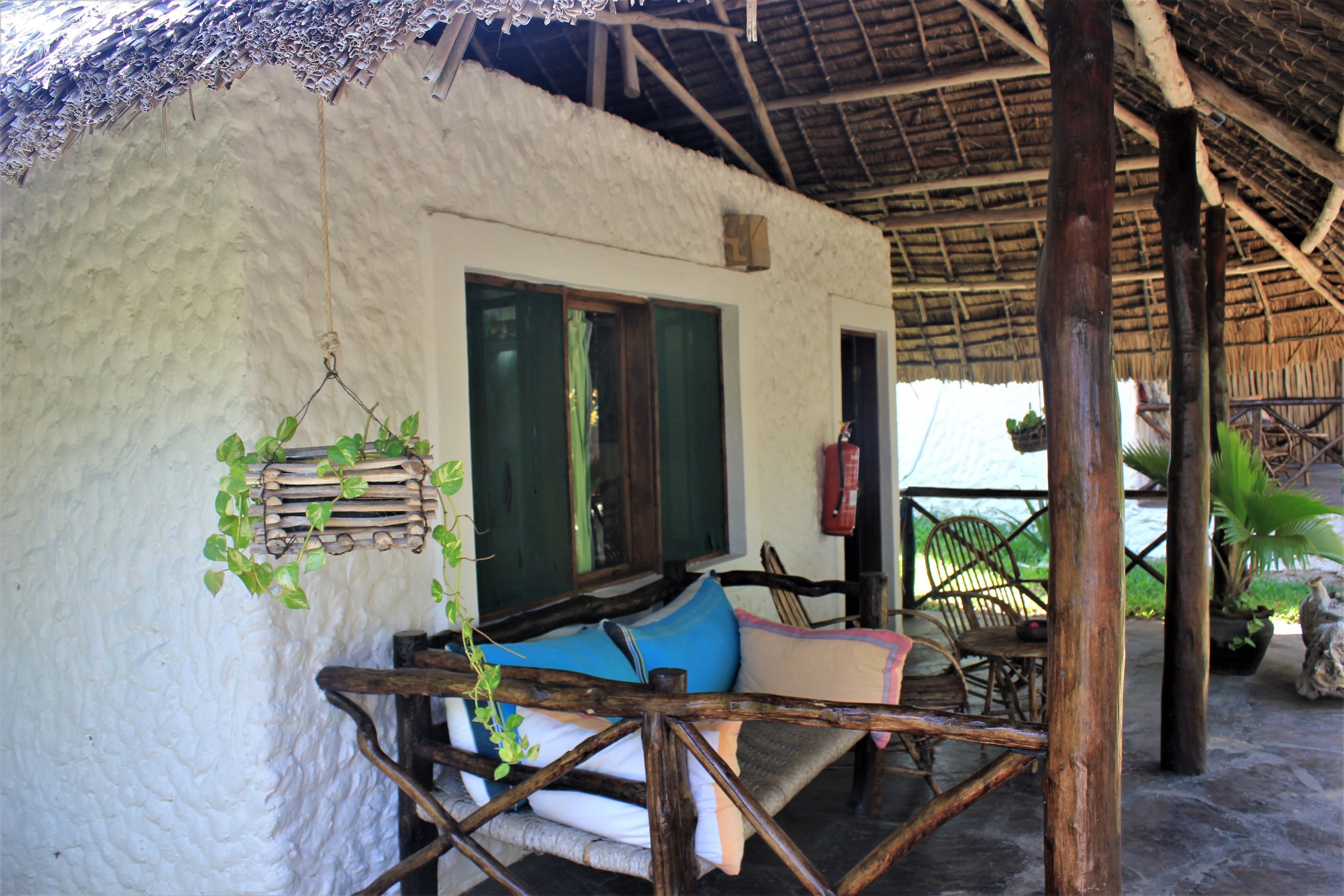 Una estructura rústica con techo de paja, una banca de madera y una ventana con cortinas.