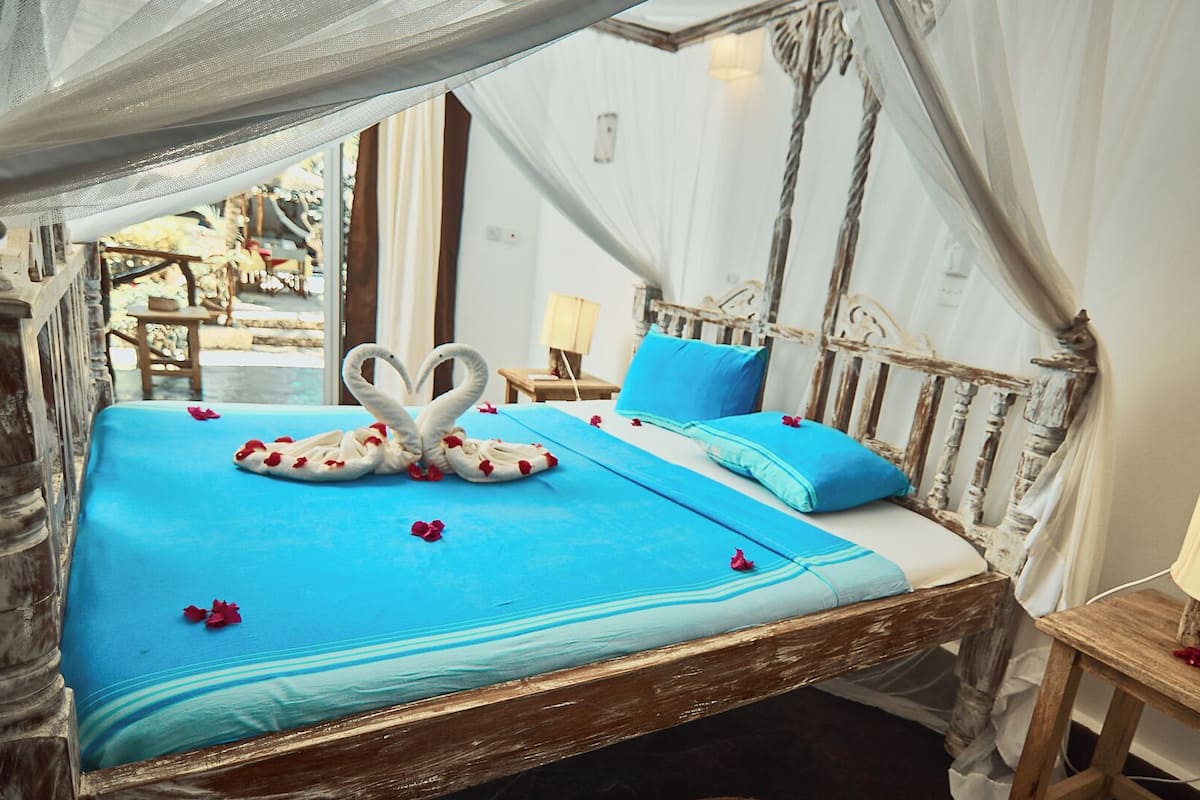 Una cama con colcha azul, una toalla dispuesta en forma de corazón y vistas al exterior.