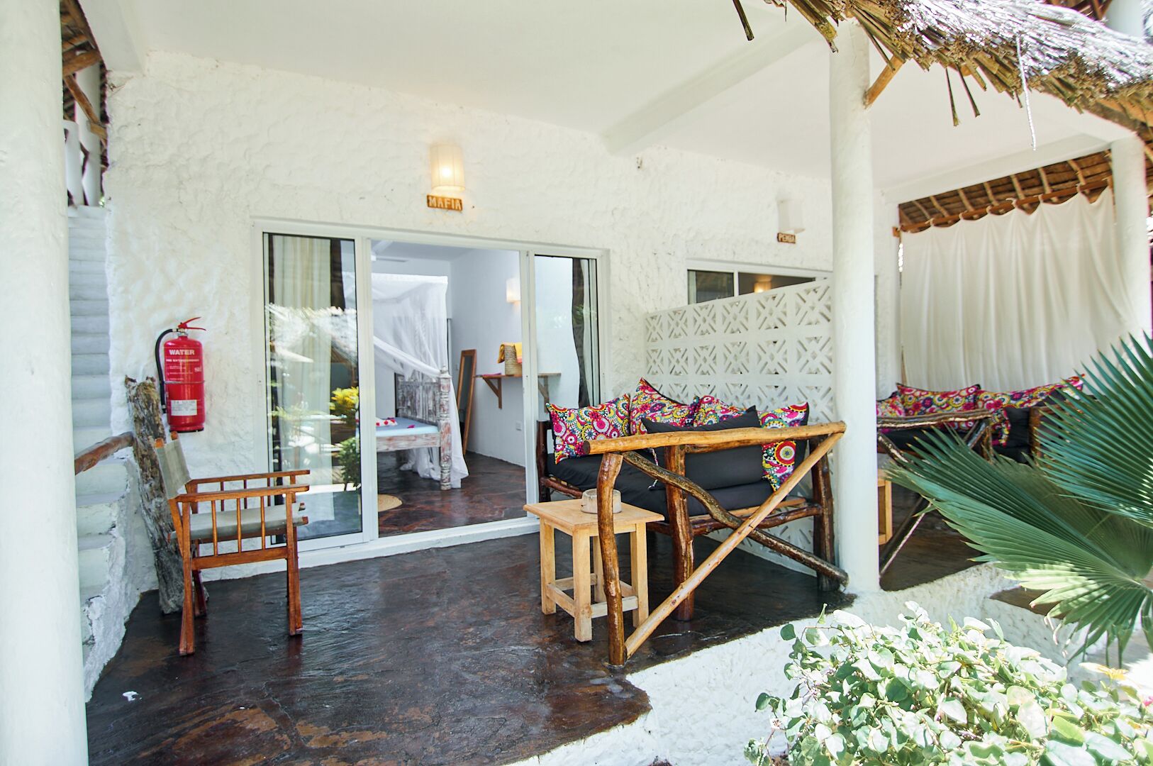 A cozy room with a wooden bench, a small table, and a bed with a canopy. There is a fire extinguisher on the wall and a plant in the corner.