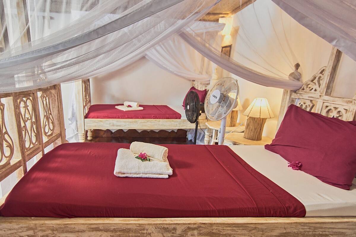 Una habitación con una cama, un ventilador, una lámpara y un adorno sobre la cama.