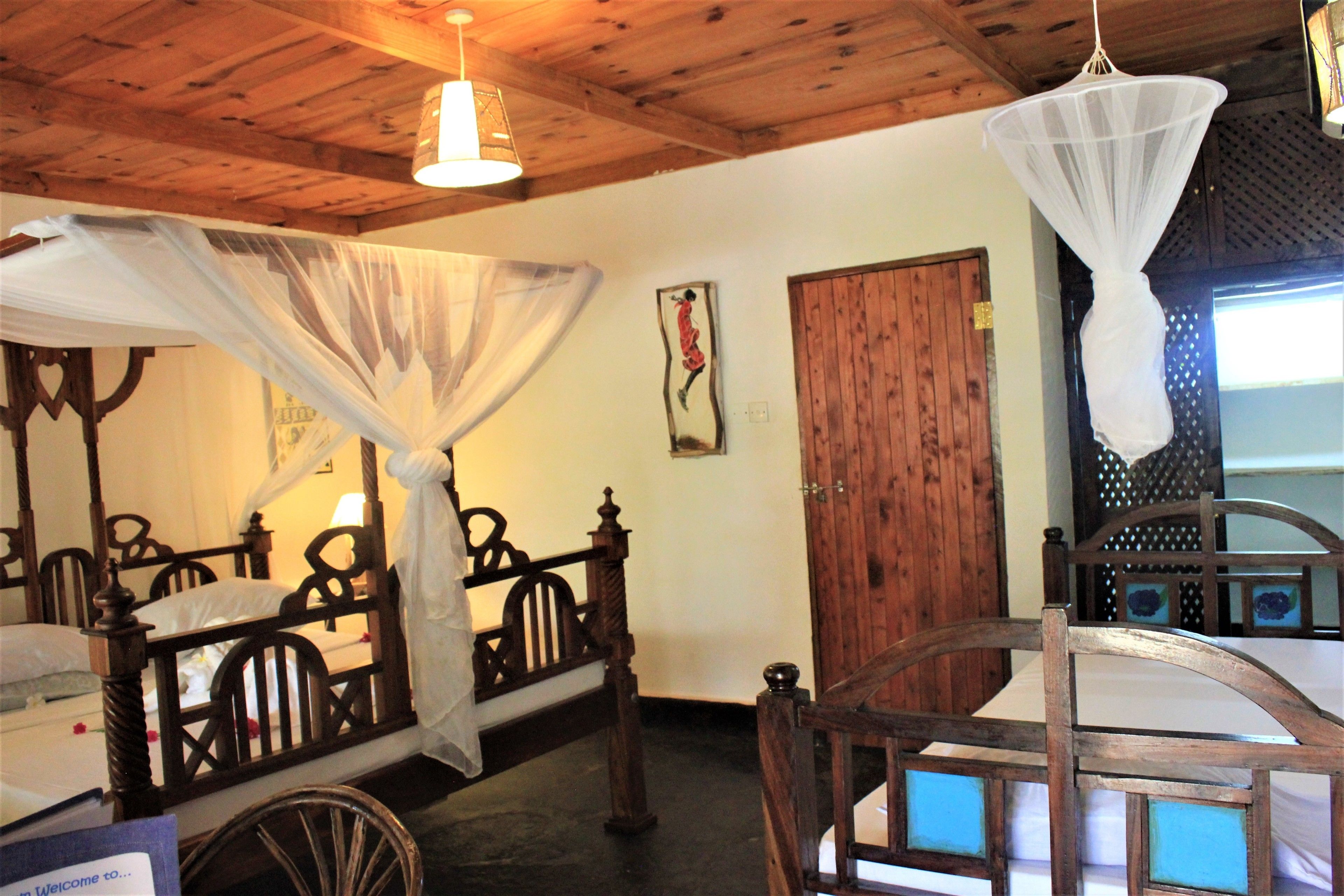 Una habitación con una cama de madera, una silla de madera, una puerta de madera y una mosquitera colgante.