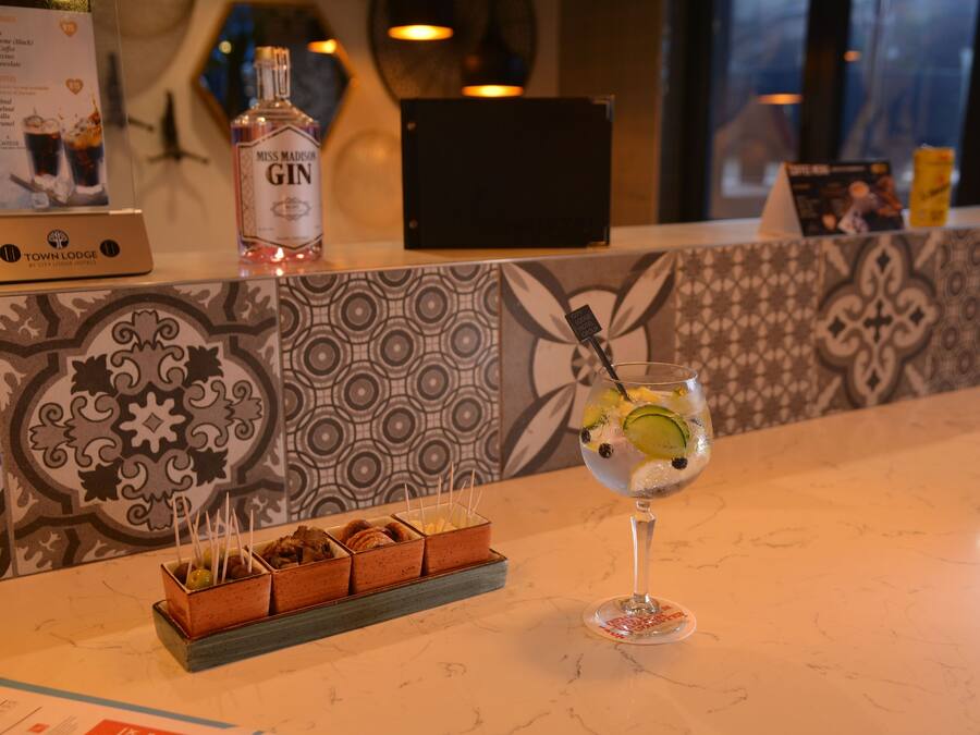 A bar area with a bottle of gin, a glass of cocktail, and a tray of snacks.