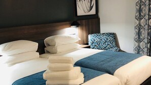 Una cama bien hecha con varias almohadas y una manta azul, un cabecero de madera, una almohada estampada y una obra de arte enmarcada en la pared.