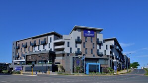 Un hotel moderno de varios pisos con un llamativo letrero de Town Lodge, que presenta una combinación de fachadas de ladrillo y cristal, y una entrada azul.