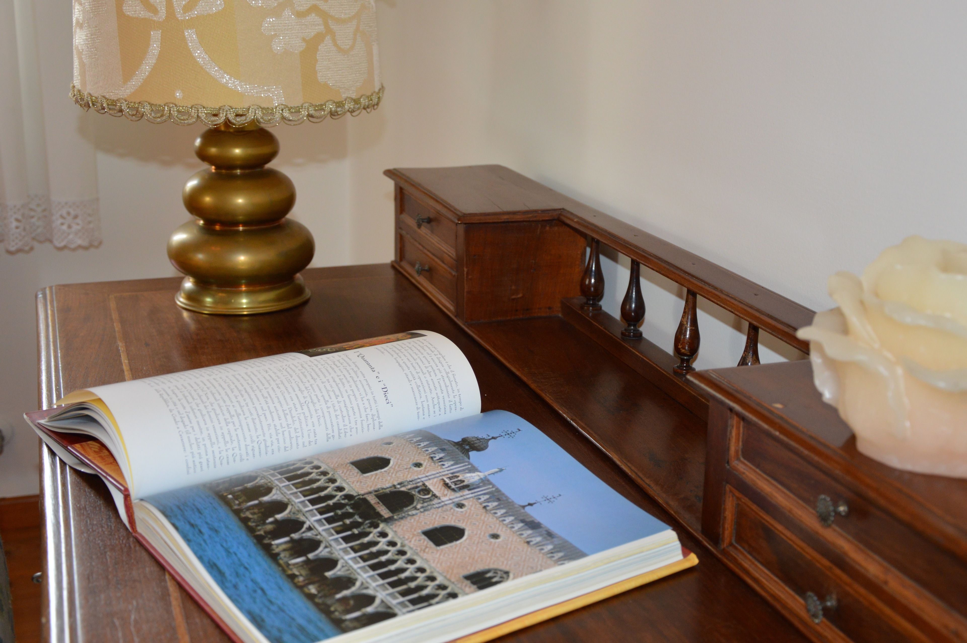A book open on a wooden table, a lamp, and a small wooden cabinet.