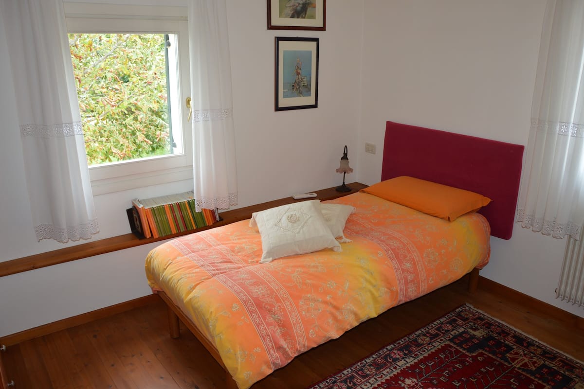 Une chambre à coucher avec un lit, une fenêtre avec des rideaux, une table de chevet et un tableau accroché au mur.