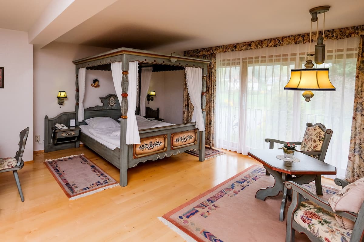 Un lit à baldaquin, un bureau en bois avec une lampe, une chaise, une table avec une lampe et une fenêtre avec des rideaux.